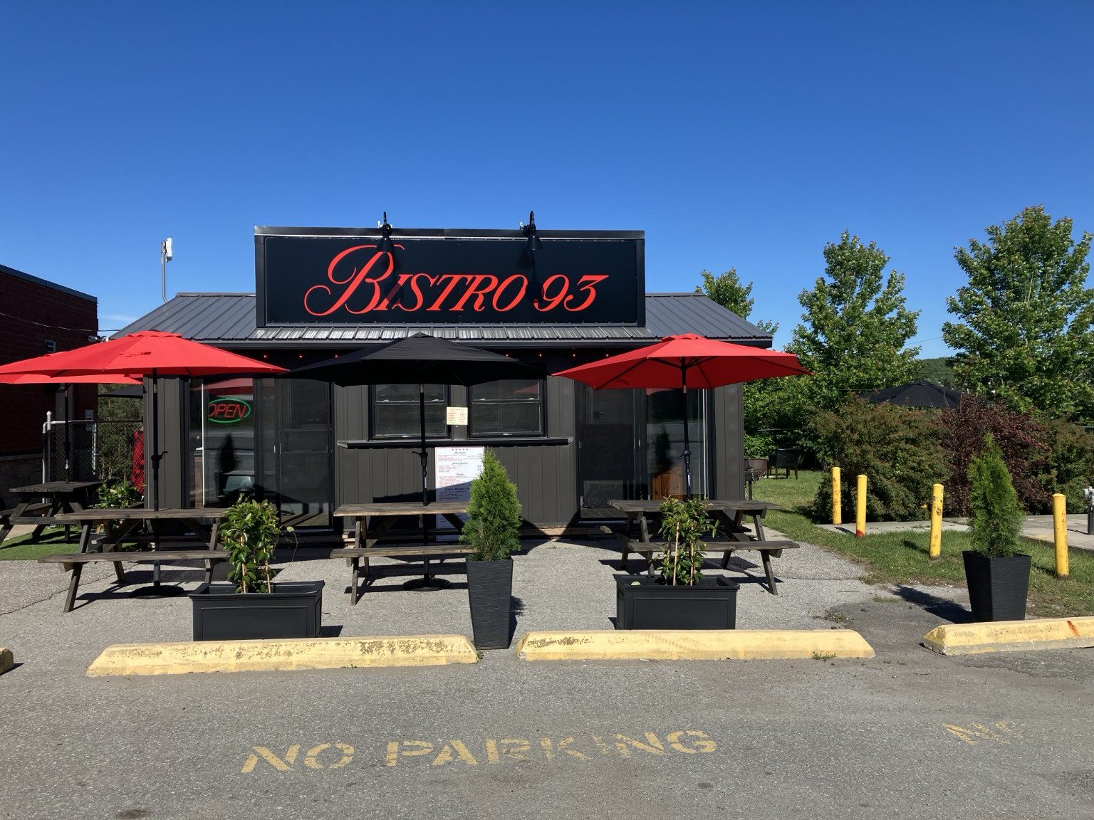 The Bistro 93 cabin with its black sign and red patio umbrellas on a sunny day